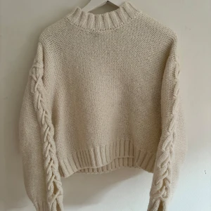 Beige stickad tröja med flätmönster - Säljer en supermysig beige stickad tröja med flätmönster längs ärmarna. Perfekt för höst och vinter! 