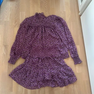 Lila blommig klänning från Neo Noir - Säljer en superfin lila klänning från Neo Noir med ett blommigt mönster. Klänningen har långa ärmar och en volangdetalj vid fållen. Perfekt för både vardag och fest!