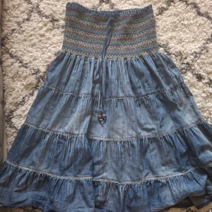 Blå jeanskjol med resårmidja - Säljer en superfin blå jeanskjol med resårmidja och färgglada sömmar. Kjolen har en volangdesign och ett knytband med träpärlor i midjan. Perfekt för både vardag och fest! 🥰