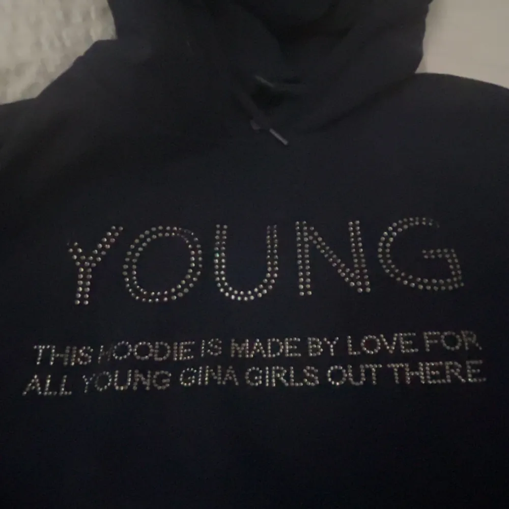 Säljer en snygg mörkblå hoodie från Gina Tricot med texten 'YOUNG' i glittriga stenar på framsidan. Perfekt för en casual look och superbekväm att ha på sig. Passar perfekt för höst och vinter! Aldrig använd endast testad.. Tröjor & Koftor.