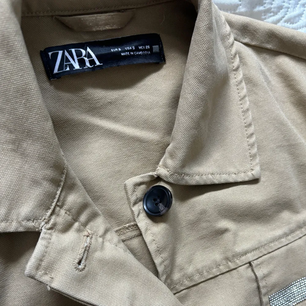 Säljer en snygg beige jacka (safarijacka) från Zara i storlek S. Jackan har långa ärmar och en klassisk krage. Den är dekorerad med glittriga detaljer på bröstfickorna och har en knappstängning framtill. Perfekt för vår och höst!. Jackor.