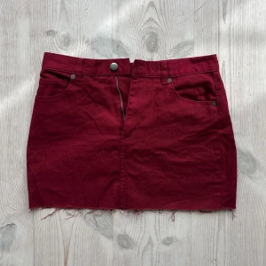 Vinröd lågmidjad jeanskjol  - Röd jeanskjol från Monki i storlek 36. Tvärs över midjan är det 36 cm och längs med sidan är det 35 cm. Har tyvärr inga bilder på då den är för liten för mig. Använd gärna köp nu!
