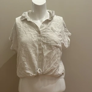 Vit blus med knyte längst ner - En vit, kortärmad blus med knyte längst ner på tröjan. Bra skick