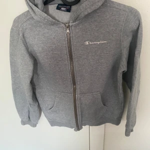 Champion huvtröja - En grå champion huvtröja med ett vitt tryck I stl 9/10 år 