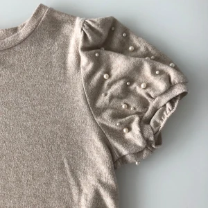 Beige tröja med pärldetaljer - Säljer en superfin beige tröja med puffiga ärmar och pärldetaljer. Tröjan är kortärmad och har en normal passform. Perfekt för både vardag och fest! 🥰