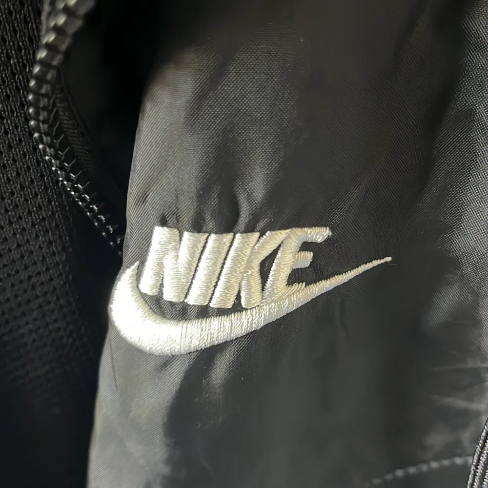 Säljer en svart vindjacka från Nike i storlek S. Jackan har en dragkedja framtill och en huva. Den är tillverkad i polyester och har en broderad Nike-logga på bröstet. Perfekt för vår och höst!. Jackor.