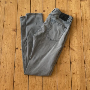 Grå jeansbyxor - Säljer ett par grå jeansbyxor i bra skick. De är slim fit och har en klassisk femficksdesign. Perfekta för både vardag och fest. Passar bra till en svart tröja eller skjorta.