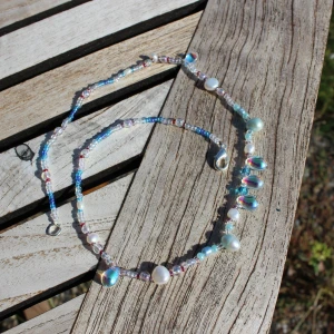 Färgglatt pärlhalsband med blå och vita pärlor - Säljer ett superfint pärlhalsband med en mix av blå och vita pärlor. Halsbandet har små, glittriga pärlor och större, skimrande pärlor som ger en härlig sommarkänsla. Perfekt för att piffa upp vilken outfit som helst! 💙✨