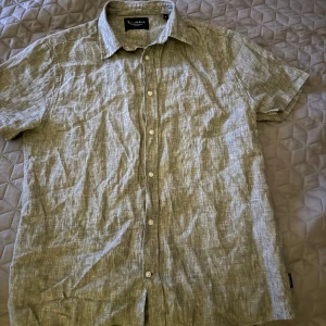 Grönaktig linneskjorta från Bondelid - Säljer en snygg kortärmad skjorta från Bondelid i storlek S. Skjortan är gjord av linne vilket gör den perfekt för varma sommardagar. Den har en klassisk krage och knappar framtill. Perfekt för en avslappnad men stilren look!