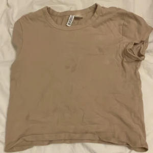 Beige t-shirt från Divided - Säljer en enkel och stilren beige t-shirt från Divided i storlek XS. Perfekt för vardagsbruk med en skön passform. T-shirten är kortärmad och gjord i mjukt material. Passar bra till både jeans och kjol!
