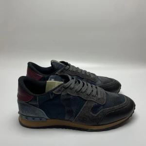 Valentino Rockrunner sneakers - Säljer ett par snygga Valentino Rockrunner sneakers i mycket bra skick. Skorna är i en cool mix av grått och svart med läder och mocka detaljer. De har en klassisk snörning och en bekväm sula som passar perfekt för vardagsbruk. Perfekta för höst och vår!