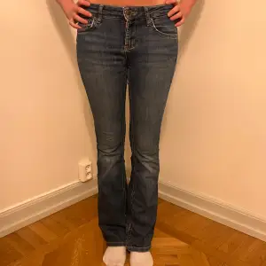 Säljer ett par snygga blå bootcut jeans i bra skick. De har en klassisk femficksdesign och är perfekta för både vardag och fest. Jeansen är midwaist och har en bekväm passform som sitter snyggt över höfterna.