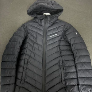 Svart dunjacka från Peak Performance - Säljer en snygg svart dunjacka från Peak Performance. Den är perfekt för kalla dagar med sin quiltade design och långa ärmar. Jackan har en praktisk huva och dragkedja framtill. Passar både till vardags och utomhusaktiviteter. Håll dig varm och stilren i vinter! 🖤nästan ny bara använd en höst 