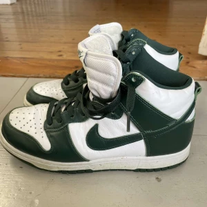 Nike Dunk i grönt och vitt - Säljer ett par Nike Dunk i grönt och vitt. Skorna har en klassisk design med snörning och är i bra skick. Perfekta för både vardag och fest. Storlek och passform är normal.
