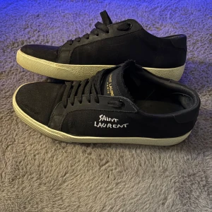 Saint Laurent skor - Säljer ett par snygga Saint Laurent skor i färgen svart i väldigt fint skick. De har en stilren design med vit text på sidan och en krämfärgad sula. Perfekta för både vardag och fest! Allt og medföljer!