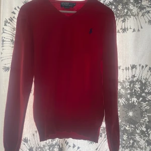 Röd tröja från Polo Ralph Lauren - Säljer en snygg röd tröja från Polo Ralph Lauren i storlek M. Tröjan har en klassisk v-ringning och är i slim fit. Den är i bra skick men har en liten lagning på ärmen från ett jättelitet hål. Perfekt för höst och vinter!