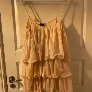 Ljusrosa volangklänning från H&M - Säljer en superfin ljusrosa klänning från H&M i storlek M. Den har tunna axelband och flera lager av volanger som ger en härlig, fladdrig känsla. Perfekt för sommarens fester eller en dag på stan. Klänningen är i mycket bra skick och redo för nya äventyr!