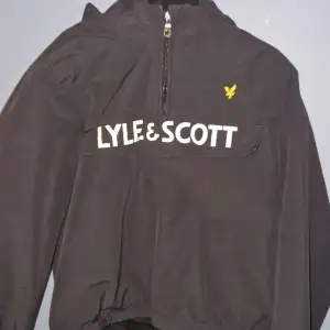 Säljer en svart vindjacka från Lyle & Scott i storlek 10/11 år. Jackan har en halv dragkedja framtill och det klassiska Lyle & Scott-logotypen på bröstet. Perfekt för höst och vår, med en stilren design och bekväm passform. Den är använd men har inga skador eller att den är smutsig. Säljer för att den inte passar längre. Pris kan diskuteras.