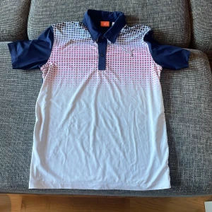 Pikétröja från Puma - Säljer en snygg pikétröja från Puma i blått och vitt med ett coolt rutmönster framtill. Tröjan har korta ärmar och en klassisk krage med knappar. Perfekt för både träning och vardag. Skön och stilren design! Pris går alltid att förhandlas!