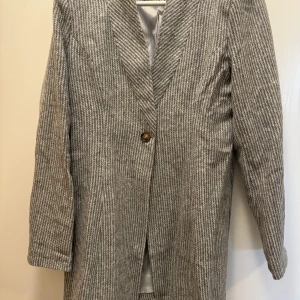 Grå randig kavaj - Säljer en stilren grå kavaj med diskreta ränder. Den har en enkel knapp framtill och är helfodrad för extra komfort. Perfekt för höst och vår, med en klassisk look som passar både till vardags och fest. Något figursydd.