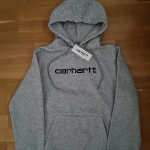 Säljer en snygg grå hoodie från Carhartt i nytt skick. Den har en klassisk design med Carhartt-loggan tryckt på framsidan. Perfekt för både höst och vinter. (Skriv innan köp)