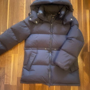 Mörkblå dunjacka från GANT - Säljer en snygg och varm mörkblå dunjacka från GANT i storlek small. Jackan har en dragkedja framtill och en mysig huva för extra värme. Perfekt för kalla vinterdagar! 🧥❄️