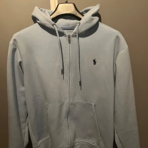 Ljusblå hoodie från Ralph Lauren - Säljer en snygg ljusblå hoodie från Ralph Lauren. Den har en dragkedja framtill och en klassisk logga på bröstet. Perfekt för både vår och höst, med en skön passform och mjukt material. Ett måste för garderoben! 💙 pris kan diskuteras 
