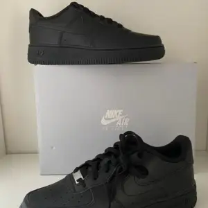 Säljer ett par klassiska svarta Nike Air Force sneakers i nytt skick. De är helt svarta med snörning och har den ikoniska Nike-loggan på sidan. Perfekta för både vardag och fest! Kommer i originalkartong.