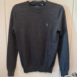 Grå tröja från Ralph Lauren - Säljer en stilren grå tröja från Ralph Lauren i merinoull. Den är i slim fit och har en klassisk design med rund hals och långa ärmar. Perfekt för både vardag och lite finare tillfällen. Tröjan är i mycket bra skick och superbekväm att ha på sig. Passar perfekt till höst och vinter!