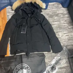 Säljer svart Canada Goose dunjacka i M. Jackan har en avtagbar huva med pälsdetalj och långa ärmar. Perfekt för kalla vinterdagar. 