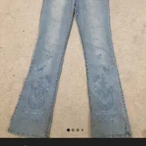 Säljer ett par ljusblå jeans med snygg broderad design på benen. De har en bootcut-stil och är perfekta för en avslappnad look. Jeansen är i bra skick och har en klassisk femficksdesign. Perfekta för både vardag och fest!