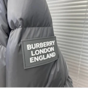 Svart pufferjacka från Burberry - Säljer en snygg svart pufferjacka från Burberry. Den är perfekt för kalla dagar med sin tjocka vaddering och stilrena design. Jackan har en dragkedja och knappar framtill samt en huva med klassiskt Burberry-mönster. Passar både till vardags och festliga tillfällen. Ops (har slarvat bort armarna)