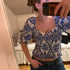 Blåvit blus med bladmönster - Säljer en superfin blåvit blus med ett snyggt bladmönster. Blusen har trekvartsärmar och en öppen rygg med knytband. säljer på grund av att den sitter lite löst då den är i storlek L