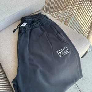 Svarta mjukisbyxor från Nike x Stussy - Säljer ett par svarta mjukisbyxor från Nike i samarbete med Stussy. Byxorna har en elastisk midja med dragsko för justerbar passform och en broderad logga på benet. Perfekta för en avslappnad stil eller träning. De är i bra skick och superbekväma!