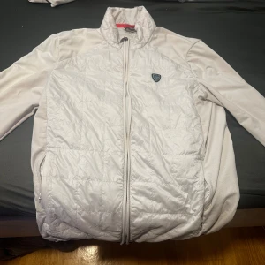 Vit jacka från Emporio Armani - Säljer en snygg vit jacka från Emporio Armani. Den har en quiltad design framtill och en dragkedja med EA7-logga. Perfekt för en stilren look! obs har lite skador men inget farlig skriv privat om ni vill ha mer bilder 