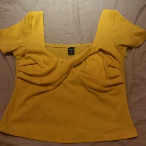 Gul ribbad topp från Shein - Säljer en superfin gul ribbad topp från Shein. Den har en snygg twist-detalj framtill och korta ärmar. Perfekt för sommardagar eller en avslappnad festkväll. Toppen är i storlek M och sitter bekvämt med en normal passform.