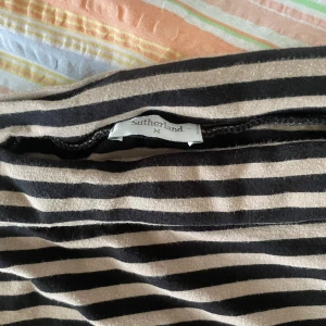 Randig kjol från Sutherland - Säljer en superfin randig kjol från Sutherland i storlek M. Den har svarta och beige ränder och är perfekt för både vardag och fest. Kjolen är kort och har en skön passform. använder som topp 