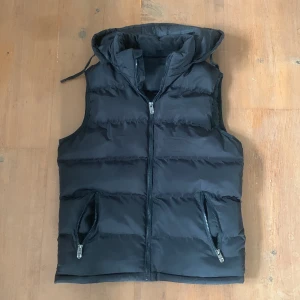 Svart väst - Hål i ena fickan, går att ta av luvan om man vill