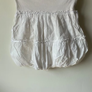 Vit klänning med volangdetaljer - Säljer en superfin vit klänning med volangdetaljer. Den har en ribbad överdel och en fluffig kjol med flera lager. Perfekt för sommarens alla fester! 💫