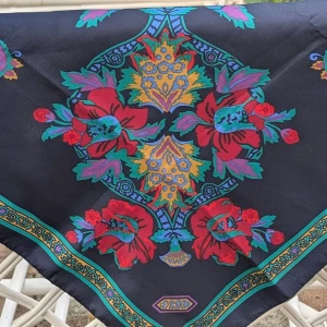 Mönstrad sjal från Totes - Säljer en snygg och färgglad sjal från Totes. Den är tillverkad i Italien och gjord av 100% polyester. Sjalen har ett vackert blommigt mönster i rött, grönt och gult mot en mörkblå bakgrund. Perfekt för att liva upp vilken outfit som helst!