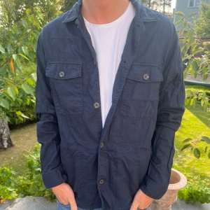 East West overshirt - Sjukt snygg mörkblå overshirt från East West. Den är storlek M och är true to size. Skicket är toppen och materialet är skönt. Enkel att matcha och ett bra plagg att ha i sin garderob. Tveka inte på att höra av er!