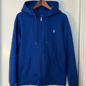 Blå hoodie från Polo Ralph Lauren - Säljer en snygg blå hoodie från Polo Ralph Lauren. Den har en dragkedja framtill och en klassisk broderad logga på bröstet. Perfekt för en avslappnad stil och passar till alla tillfällen. Den är i bra skick och superbekväm, Storlek S men även M.