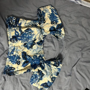 Blommig topp med puffärmar - Säljer en superfin blommig topp med puffärmar. Den har en härlig kombination av blå och beige färger med ett vackert blommönster. Perfekt för sommardagar eller en festlig kväll! Använt 2-3 ggr.