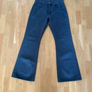 Svarta/gråa jeans från Acne Studios - Säljer ett par snygga svarta jeans från Acne Studios. Modell är 1992m Faded black. De är högmidjade och har en bootcut-stil som ger en riktigt trendig look. Jeansen är tillverkade i 100% bomull vilket gör dem både bekväma och hållbara. Perfekta för både vardag och fest!