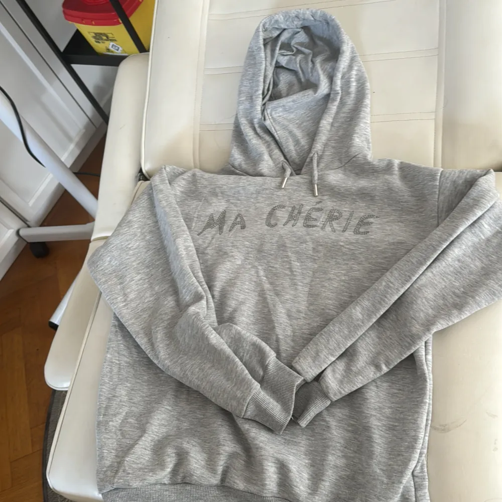 Säljer en supermysig grå hoodie från Gina Tricot i storlek XS. Den har texten 'MA CHERIE' tryckt på framsidan och en klassisk huva med dragsko. Perfekt för en chill dag eller när du bara vill vara bekväm. Den är i bra skick och redo för en ny ägare!🩶. Hoodies.