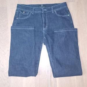 Jeans från Jeans by Bessie - Säljer ett par snygga jeans från Jeans by Bessie, tillverkade i Italien. De är mörkblå med klassisk femficksdesign och har en snygg detalj på bakfickan. Perfekta för både vardag och fest!