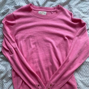 Rosa tröja med knappar - Säljer en superfin rosa tröja i mjukt material. Den har långa ärmar och snygga knappar vid ärmsluten och nederkanten. Perfekt för både vardag och fest! 💖