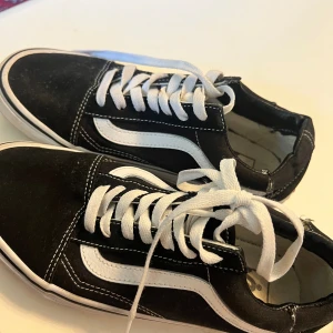 Svarta Vans sneakers - Säljer ett par klassiska svarta Vans sneakers med vit sula och vita snören. Skorna har den ikoniska vita sidostripen och är i välanvänt skick. Perfekta för en avslappnad stil. skorna är använda och lite slitna på bilden som ni ser men annars funkar jätte bra!