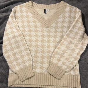 Beige och vit stickad tröja från Hm - Säljer en superfin beige och vit stickad tröja från H&M . Den har ett klassiskt hundtandsmönster och en bekväm v-ringning. Perfekt för höst och vinter! Tröjan är i nyskick och har ribbade muddar vid ärmslut och nederkant. Passar perfekt för en mysig dag hemma eller en promenad i parken. 🍂