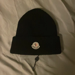 Monclear mössa  - En äkta monclear mössa i nyskick, med monclear klistermärket kvar på lappen i mössan som bevis på att den är ny. Köpt för 2000 kr, säljer för 400 kr men pris kan diskuteras.
